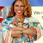 Smiling maker in a floral outfit cradling an armful of jar candles in front of stocked candle shelves