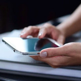 Close-up of two hands holding a smartphone over a dark surface
