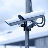 White outdoor surveillance security camera mounted on a metal pole against a pale sky