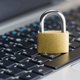 Brass padlock standing closed on a black laptop keyboard