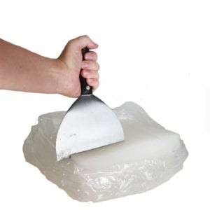 Hand using a metal scraper to break up a plastic-wrapped slab of paraffin wax