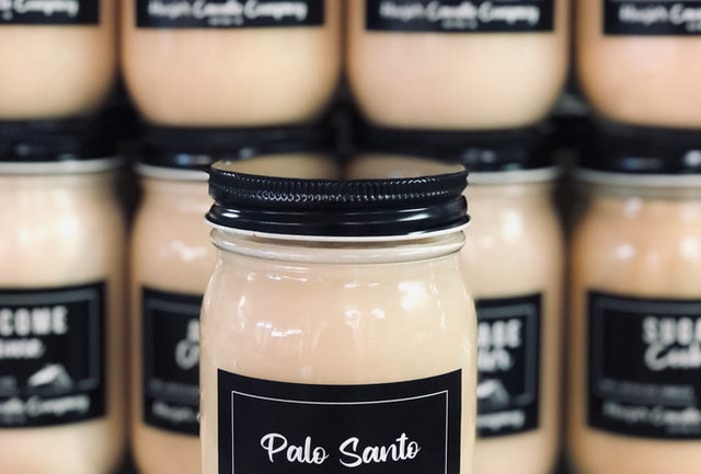A Hoosier Candle Company Palo Santo mason-jar candle in front of rows of matching black-labeled jar candles