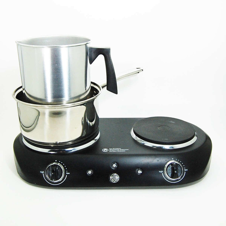 Stainless pouring pot nested in a saucepan double boiler on a black two-burner hot plate