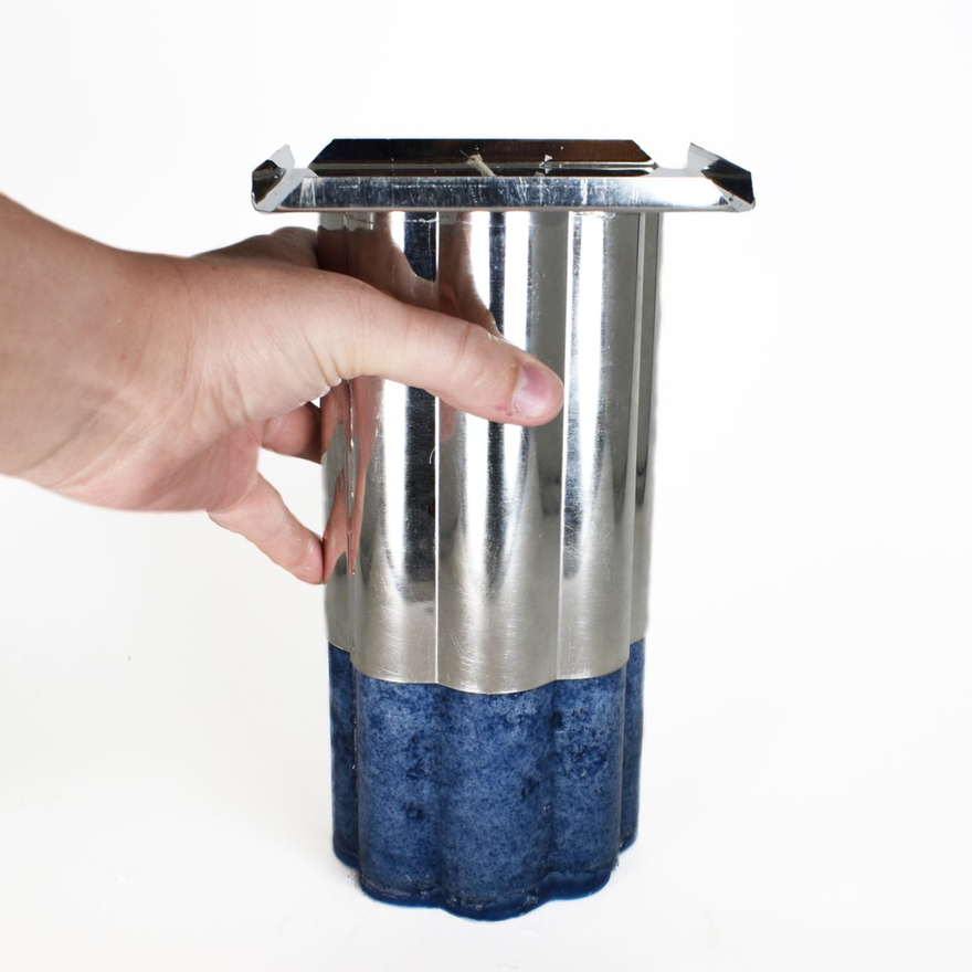 Hand holding upended fluted pillar mold with the blue candle sliding partway out