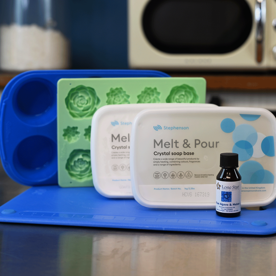 Blue round mold, green succulent silicone mold, two tubs of Melt & Pour crystal soap base, and a fragrance oil bottle on a counter