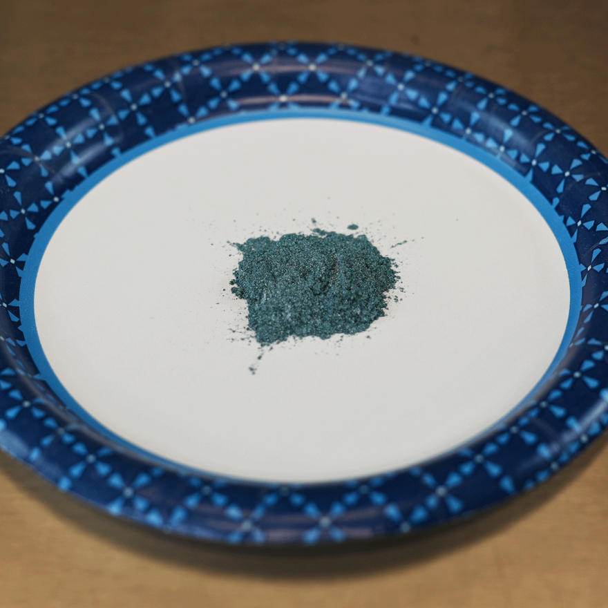 Small pile of teal mica powder on a white paper plate with a blue plaid rim
