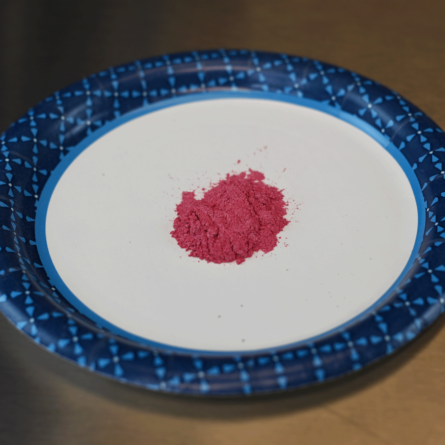 Small pile of pink mica powder on a white paper plate with a blue plaid rim