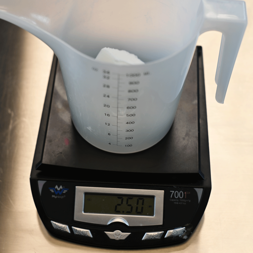 Plastic measuring jug of white soap base chunks on a digital scale reading 250 grams