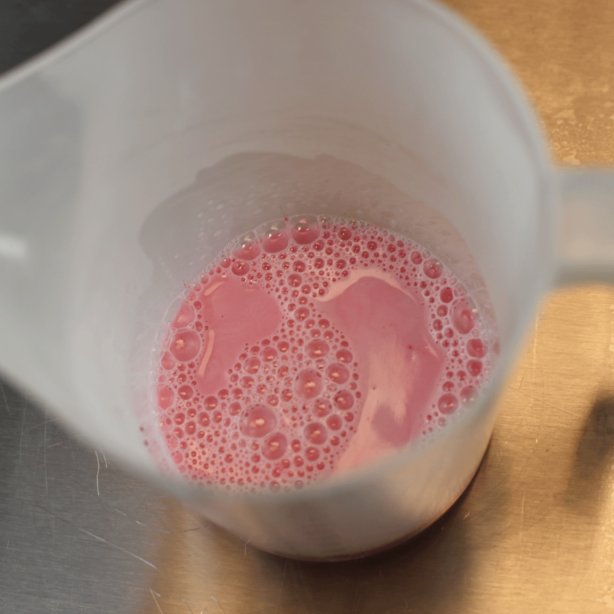 Plastic measuring jug holding melted pink soap with foamy bubbles on top