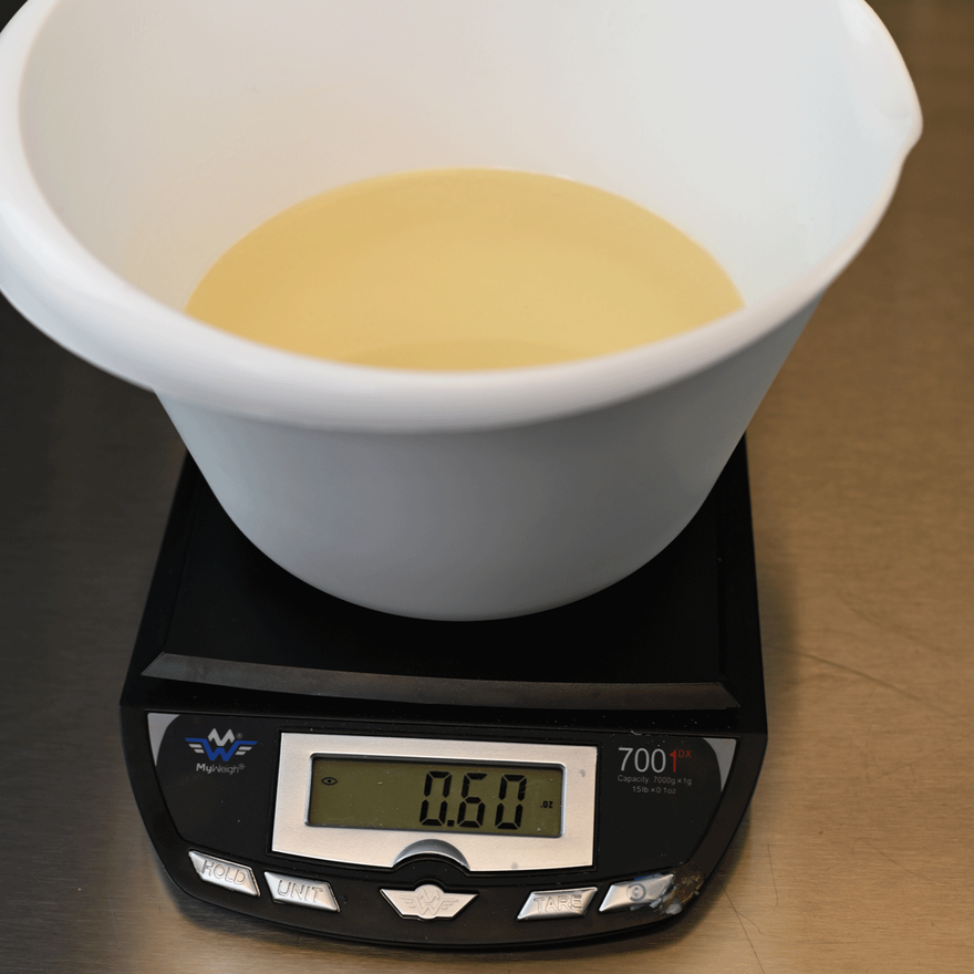 White bowl of melted clear amber soap on a digital scale reading 60 grams