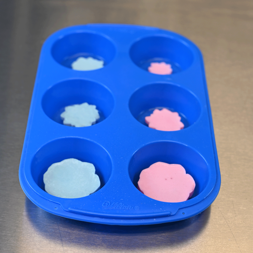 Blue and pink succulent soap embeds placed in cavities of a blue silicone muffin mold