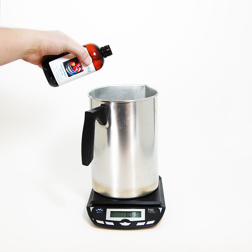 Hand tipping a Lone Star Georgia Peach fragrance bottle over a pouring pitcher on a scale