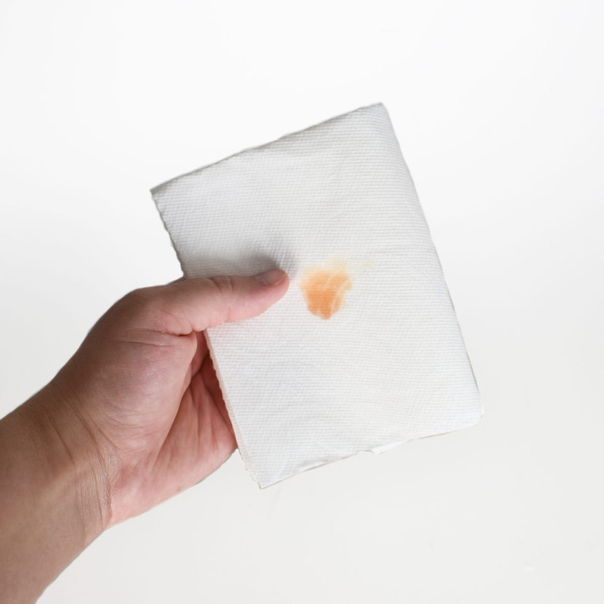 Hand holding a folded paper towel with a faint orange wax smear color test