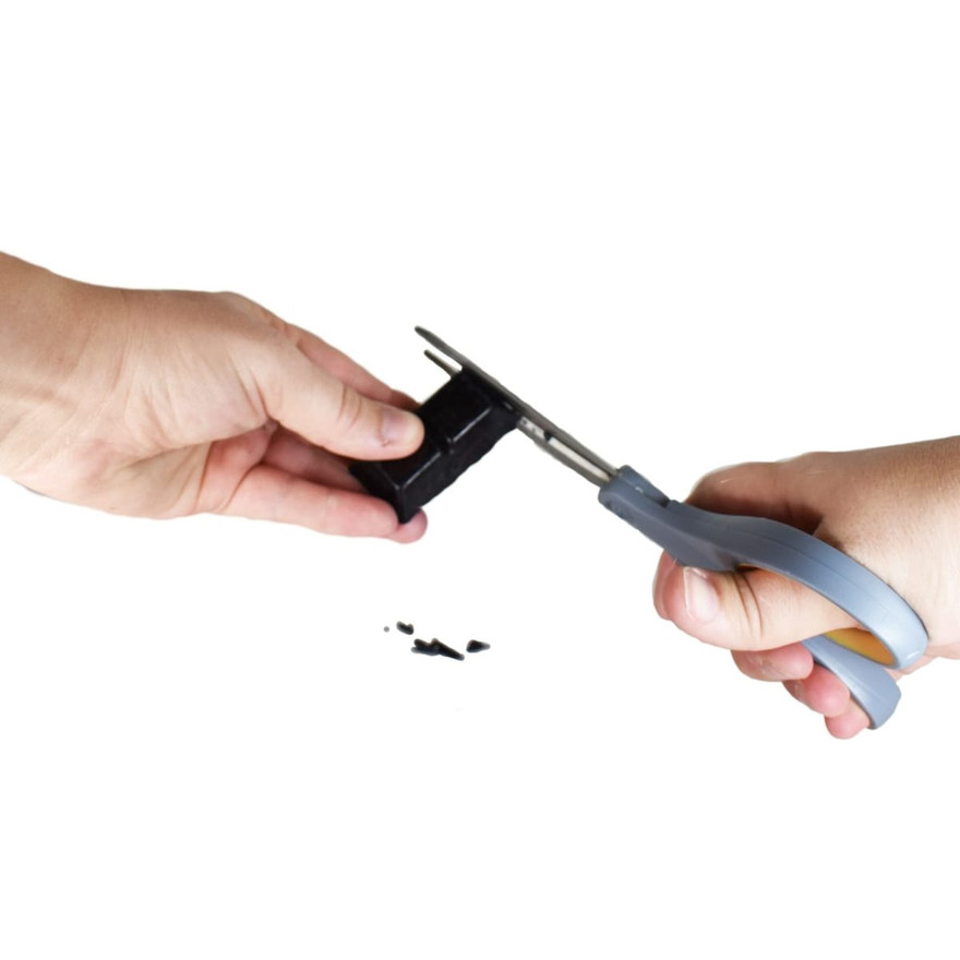 Two hands snipping shavings off a black dye block with scissors over a white surface